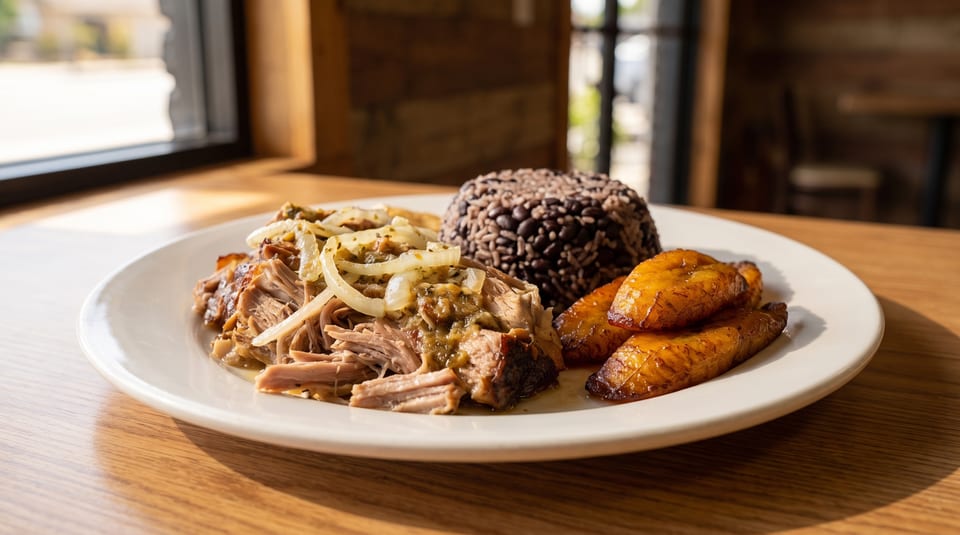 Cuban mojo pork with onions, black beans and rice, and fried plantains on a white plate.