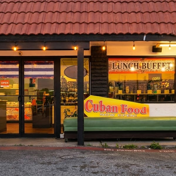 Exterior of a Cuban restaurant with a red tile roof, an "OPEN" sign, and a green bench.