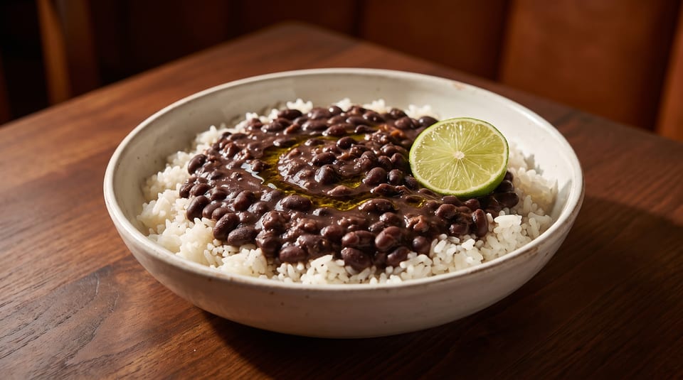 A bowl of white rice topped with black beans, olive oil, and a lime wedge.
